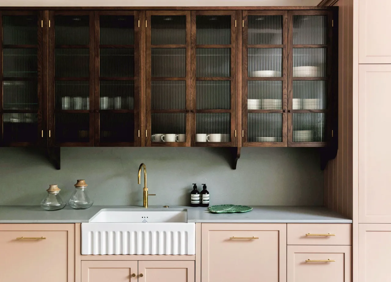 Blush-painted lower cabinets sit beneath dark wood glass-front uppers