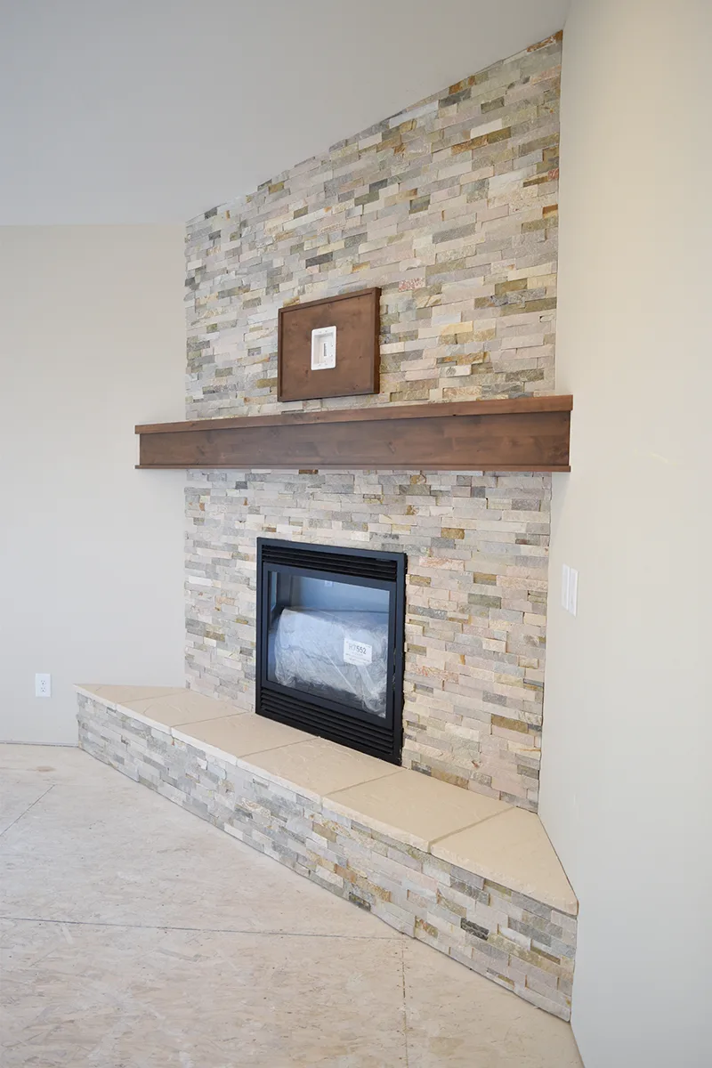 Tall pale textured corner fireplace with a broad wood mantel, small framed picture and angled hearth.