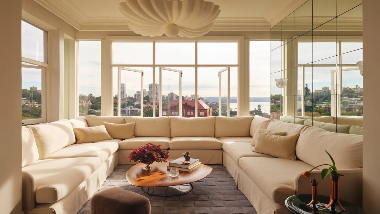A pale corner sofa sits beneath broad windows beside a simple central table.