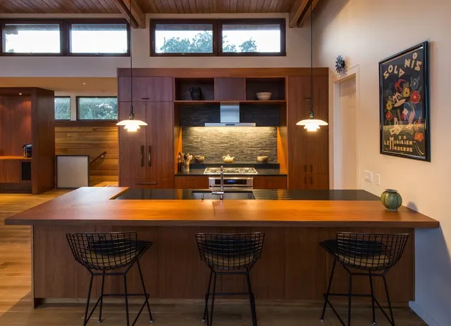 A long timber breakfast bar faces a wood cabinet wall with a darker backsplash.