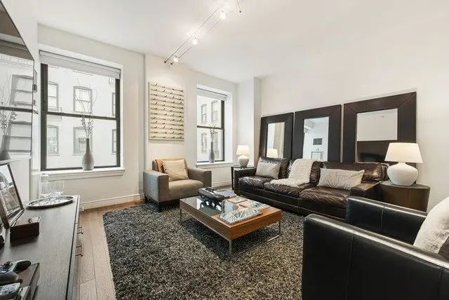 A deep leather sofa sits beside pale upholstered seating beneath a broad dark mirror.