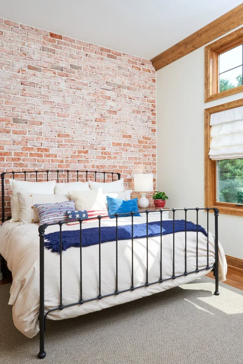 Bedroom with red brick-pattern wall, dark spindle bed, wood window trim and blue bedding accents