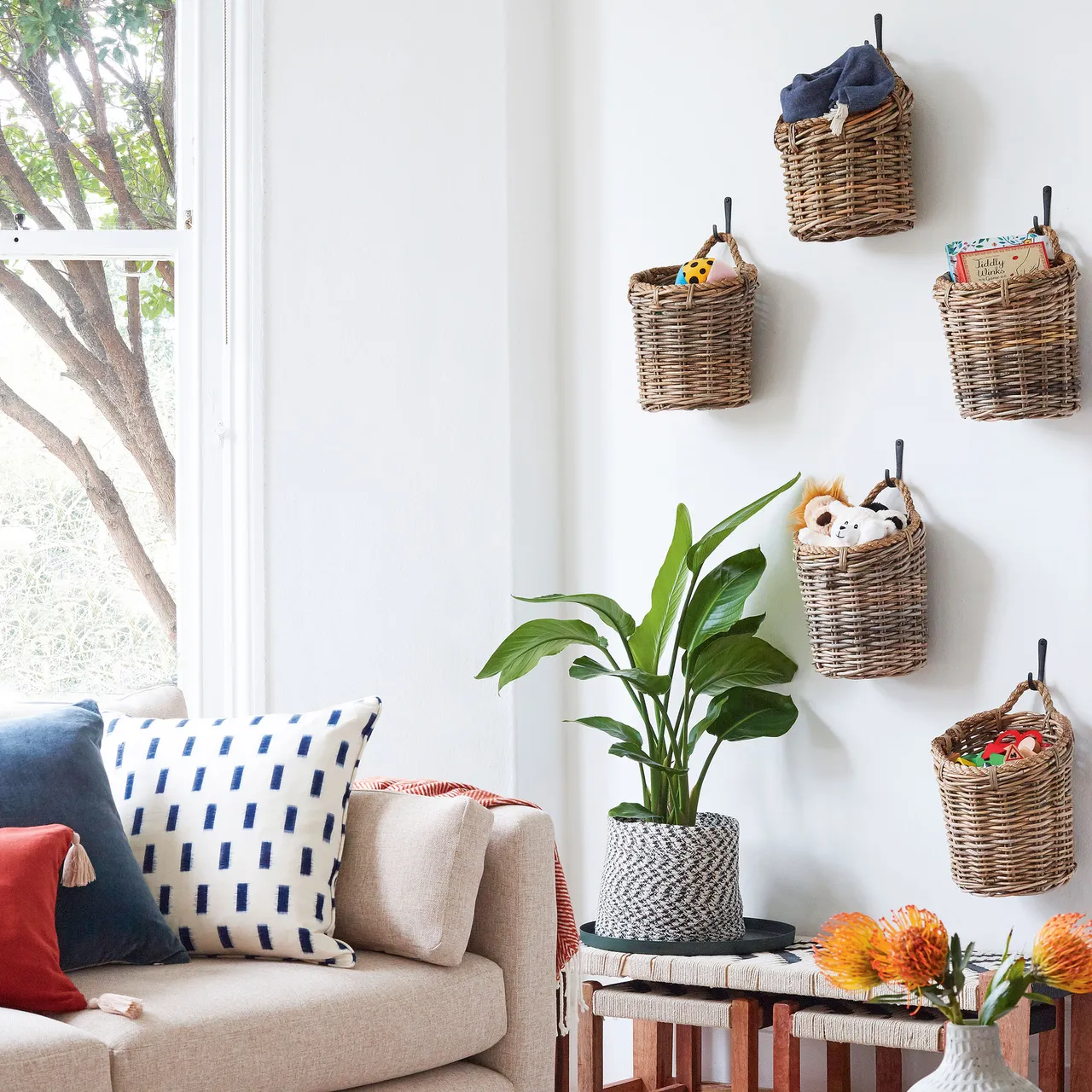 Woven baskets hang beside a window near pale seating and a small table