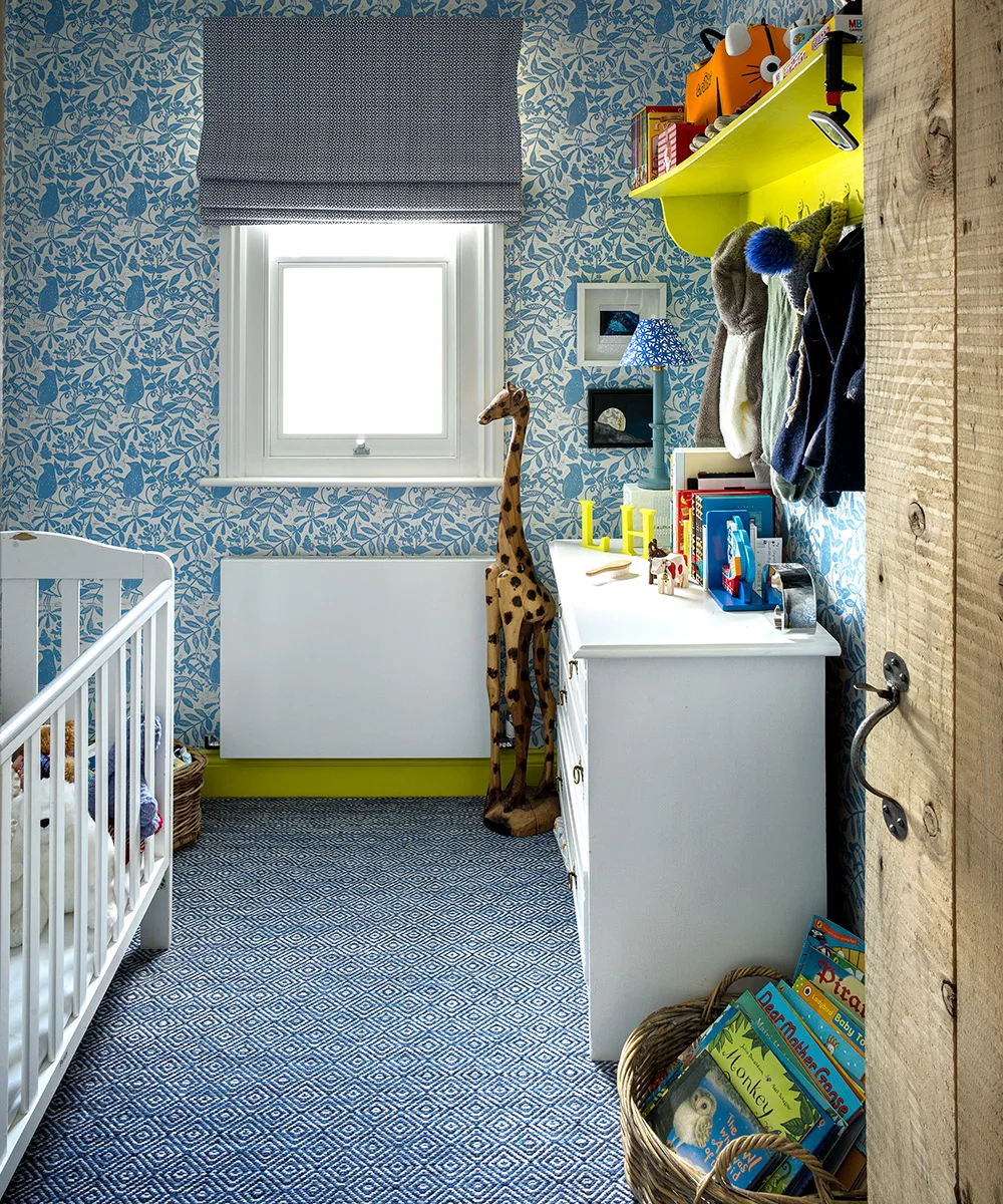 Blue botanical nursery wallpaper meets a fine geometric blue floor, gray patterned blind and bright yellow-green shelf above a white dresser