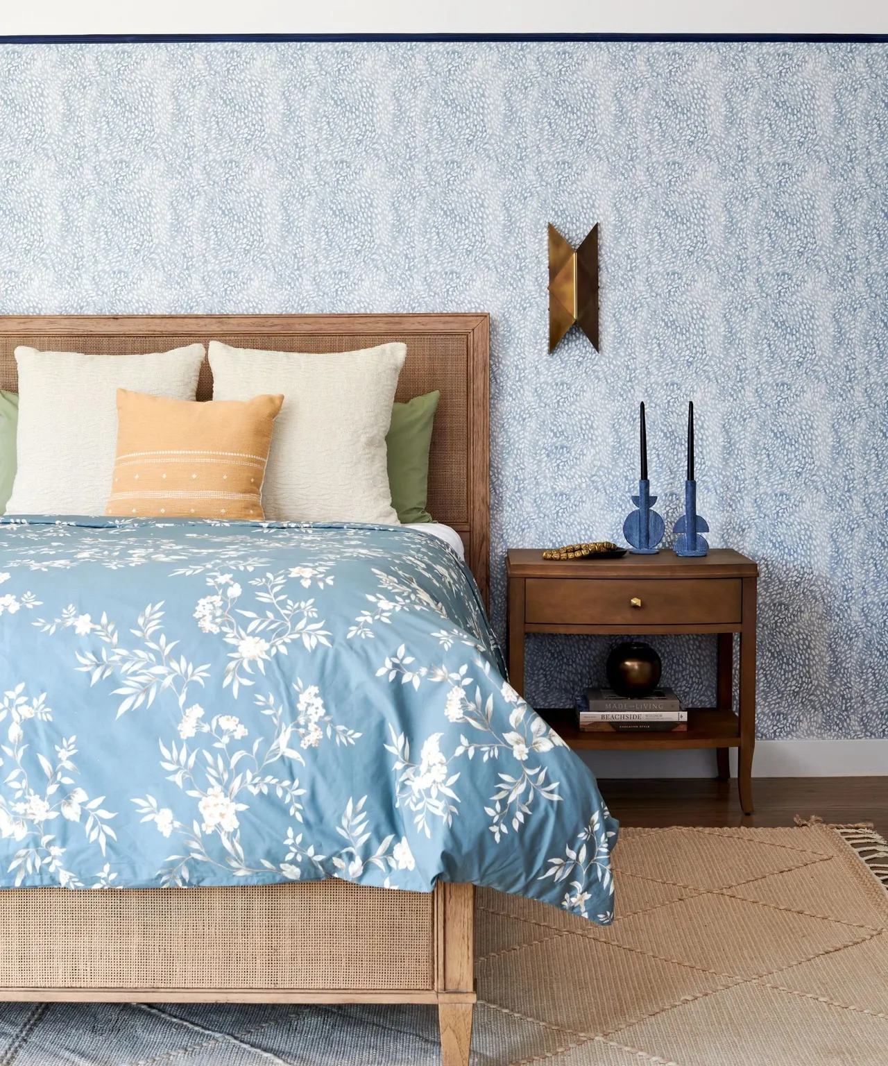 Pale blue patterned walls sit behind a timber bed with blue-and-white bedding and warm pillows.