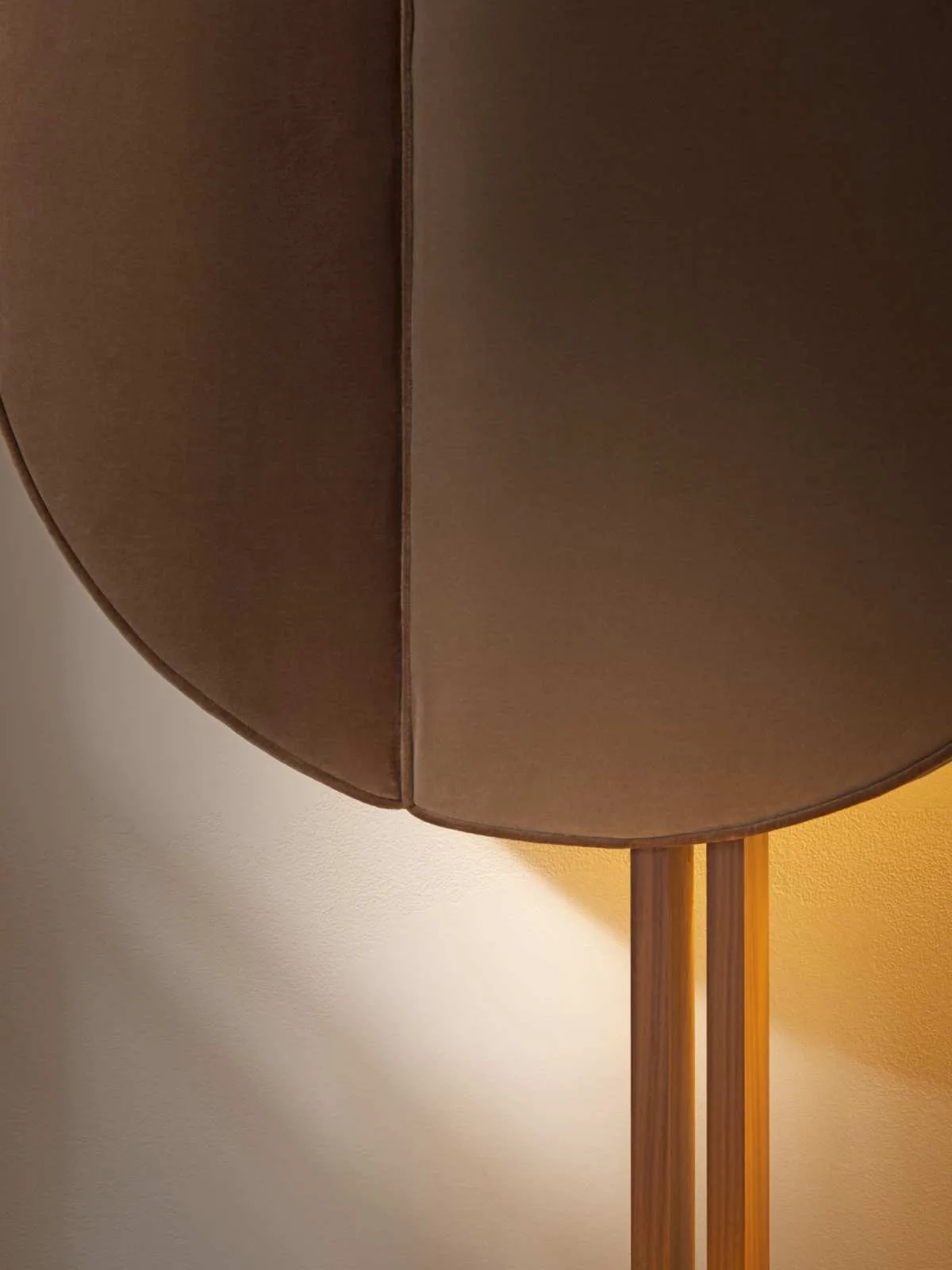Close photograph of a curved padded headboard section with stitching, a wood support and warm light behind it.