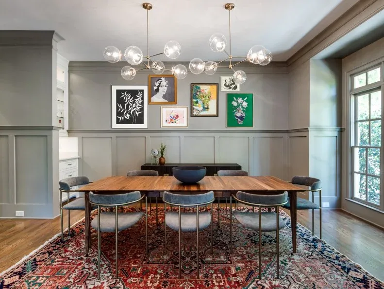 Gray dining room with broad rectangular lower-wall panels, a picture group, wood table and clear globe chandelier
