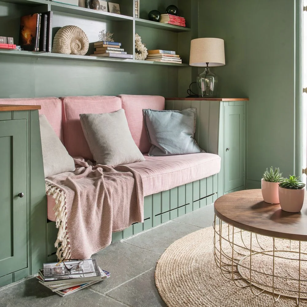 Pink bench cushions sit within green built-in seating and open shelves beside a round coffee table