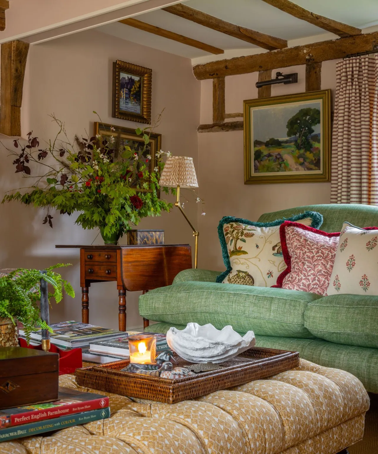A soft green sofa sits beneath timber beams beside woven furniture and fresh foliage.