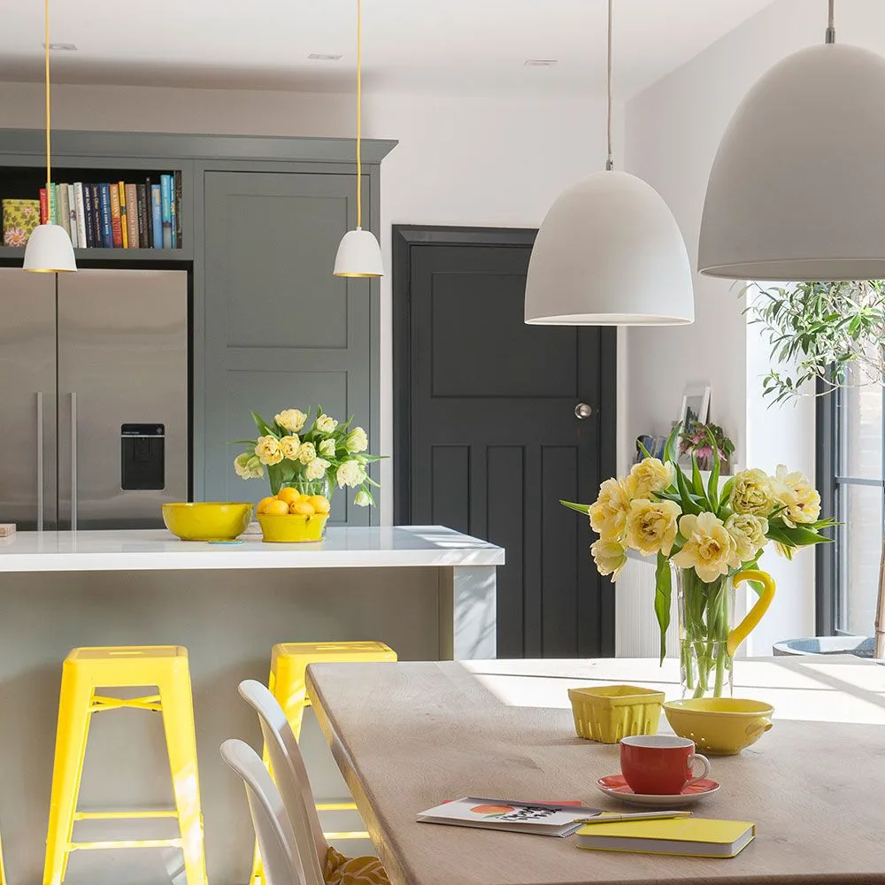 Two large white domes above a dining table with smaller white lights over the kitchen island behind