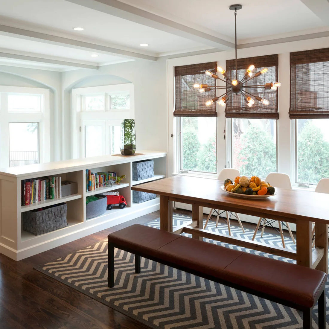 Low white cubby shelving with books and baskets beside a wood dining table and long upholstered bench