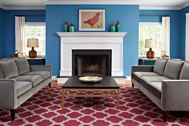 Rich blue walls surround a pale fireplace between matching windows and gray seating.
