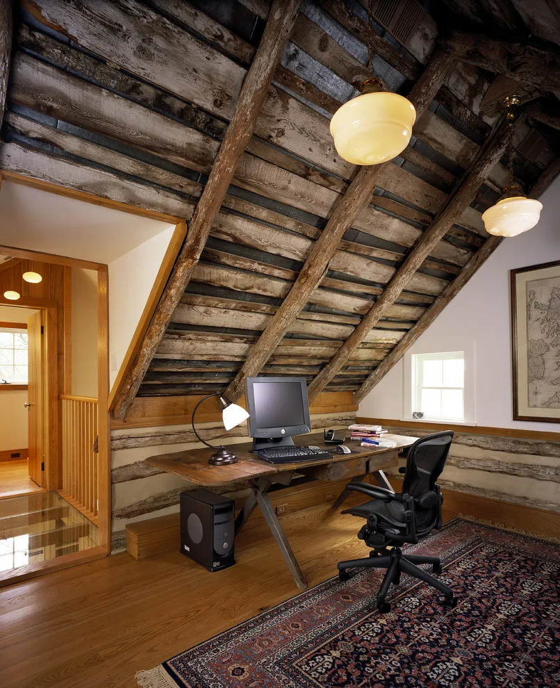 A rough timber desk sits beneath a steep wooden roof beside a window