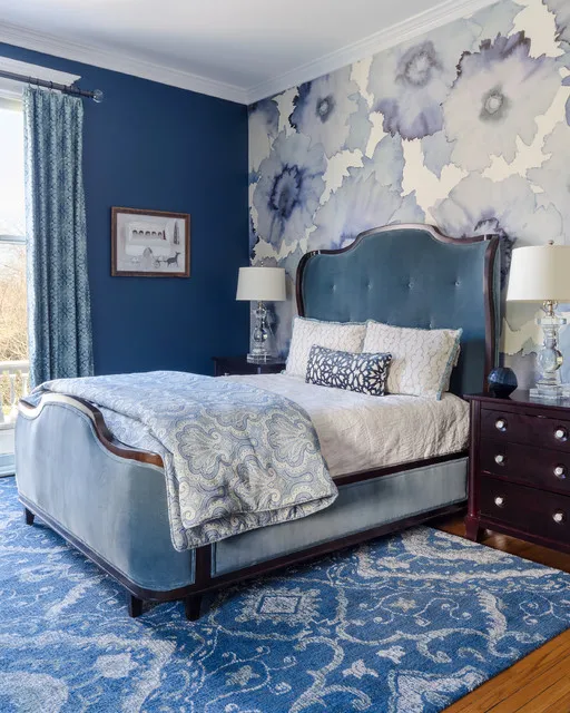 A large pale floral pattern rises behind a blue headboard beside a darker blue wall.