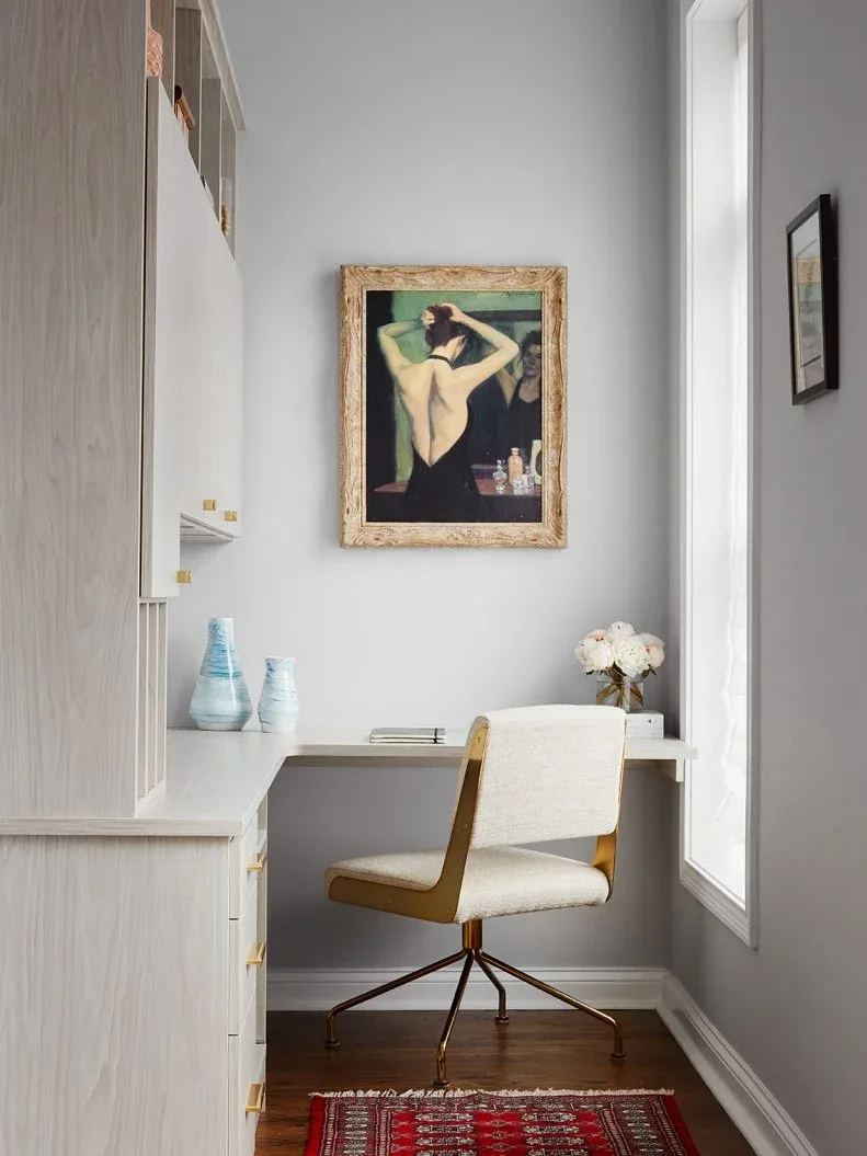 Pale built-in desk niche with a white upholstered chair on a warm metal frame and gold-toned cabinet handles.