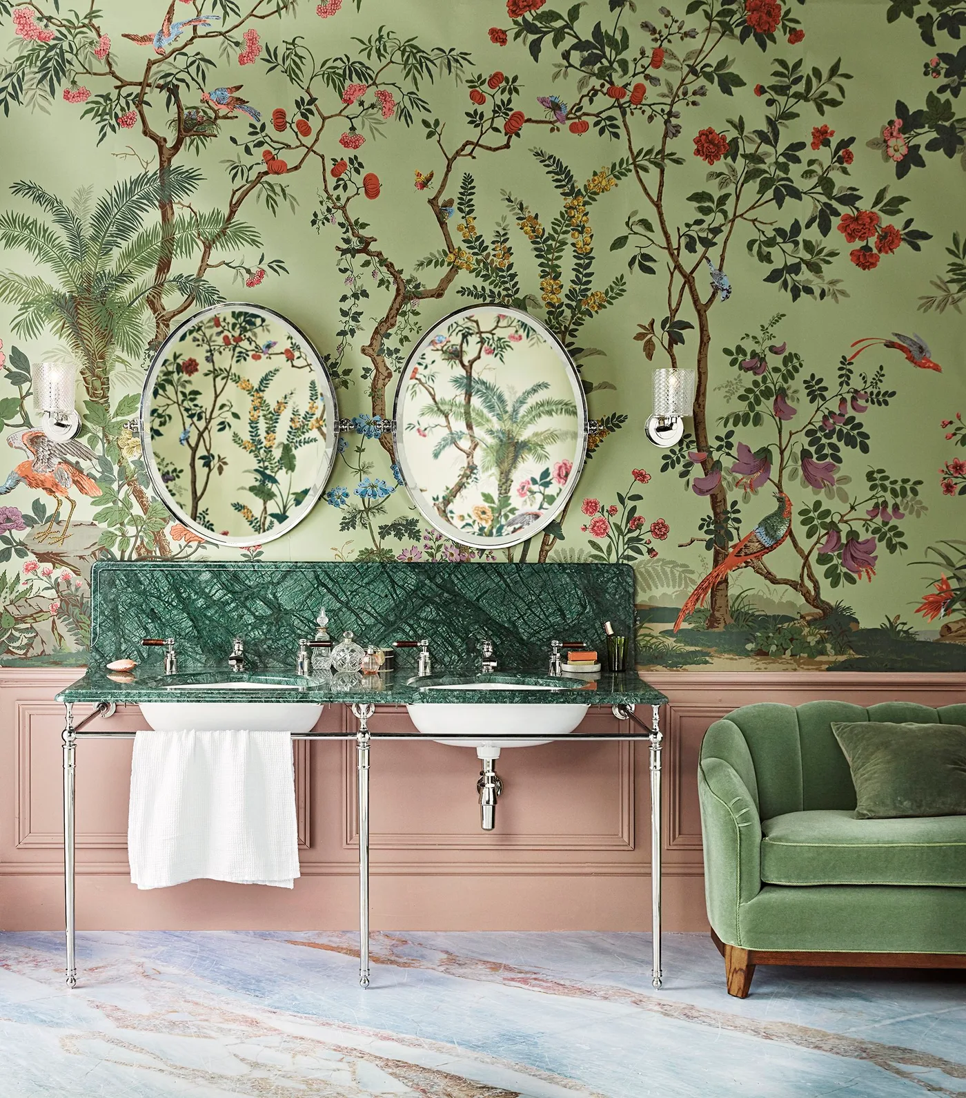 Double console basin with a green veined backsplash, round mirrors, floral wallpaper and pink lower wall paneling.