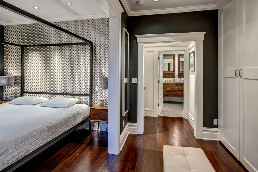 A reddish dark wood floor runs beside a black-framed bed and patterned wall