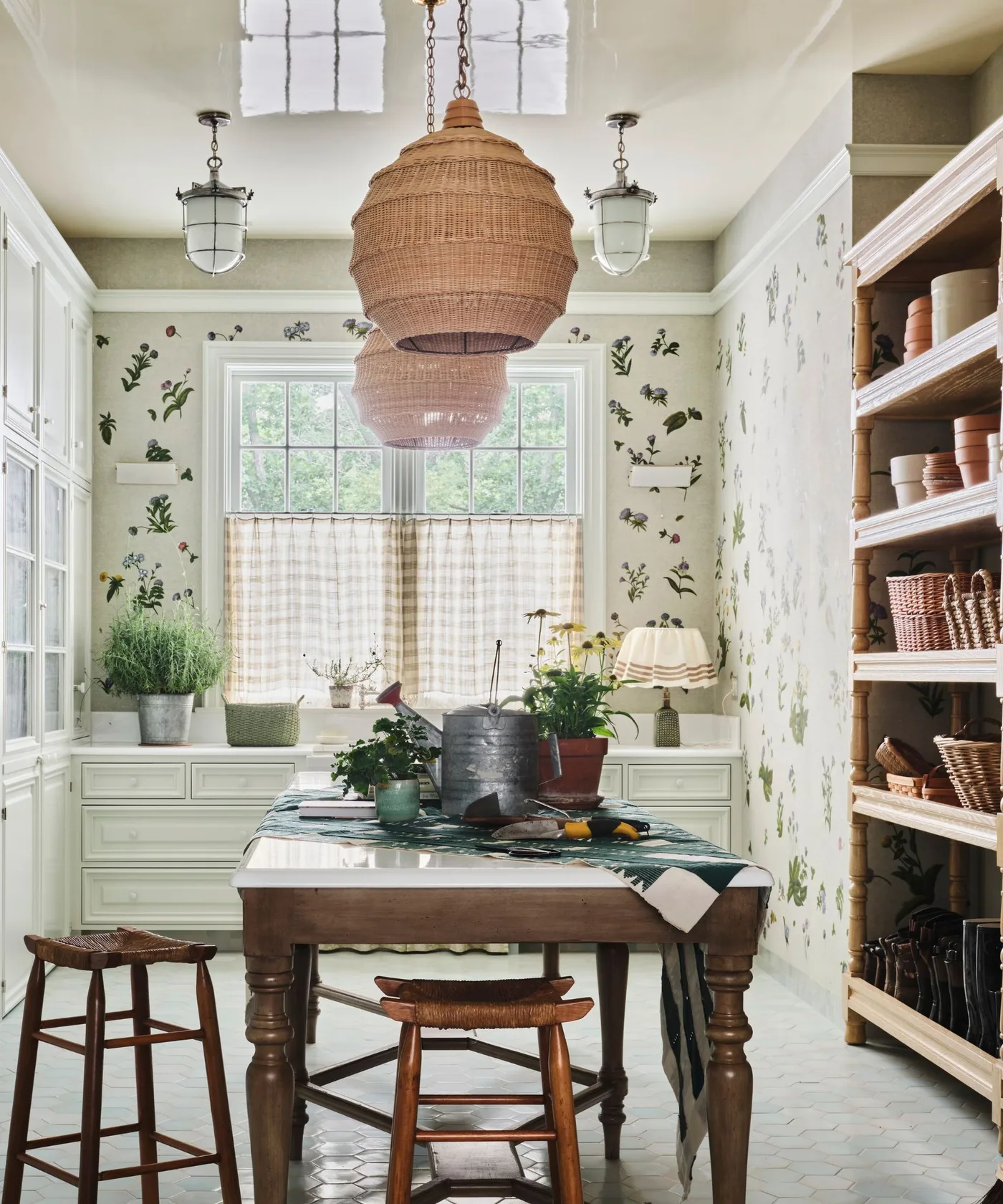 Country kitchen dining corner with loose floral wallpaper, pale cabinetry, wood table and woven pendant