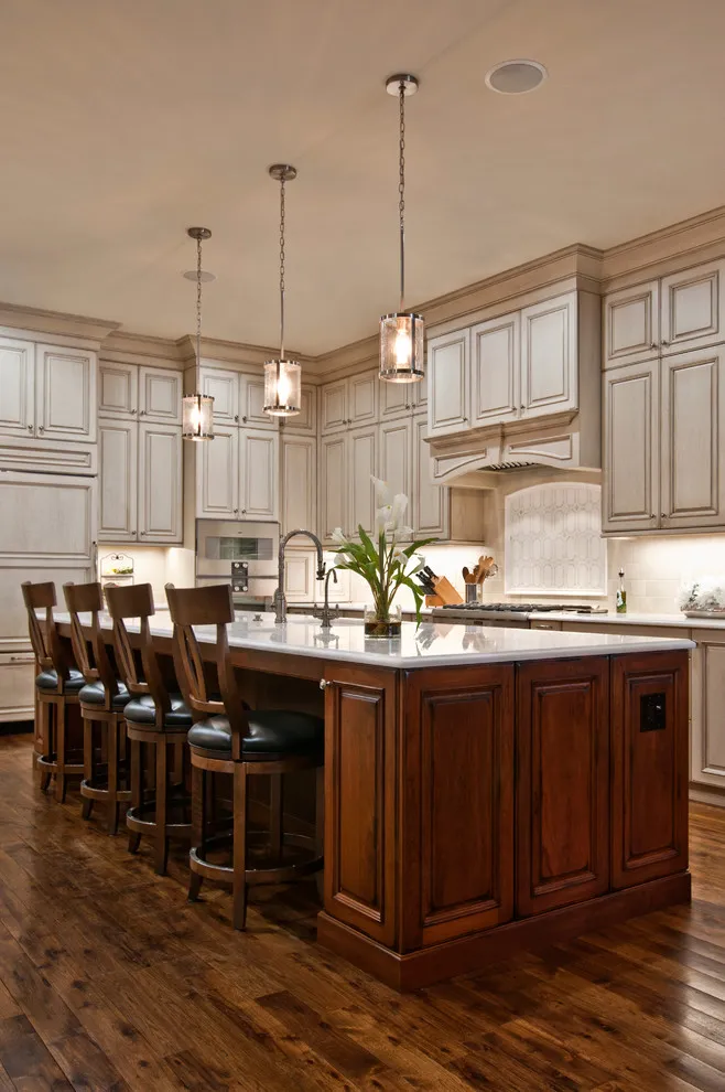 Pale paneled cabinets surround a timber island with dark upholstered wooden stools