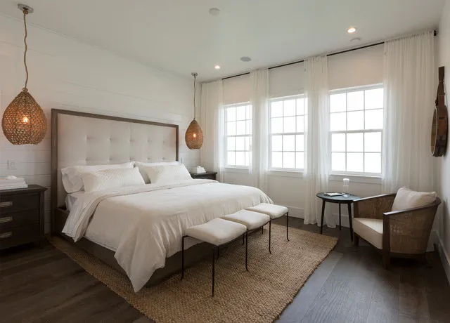 Three small pale upholstered benches at the foot of a light bed beneath woven pendants