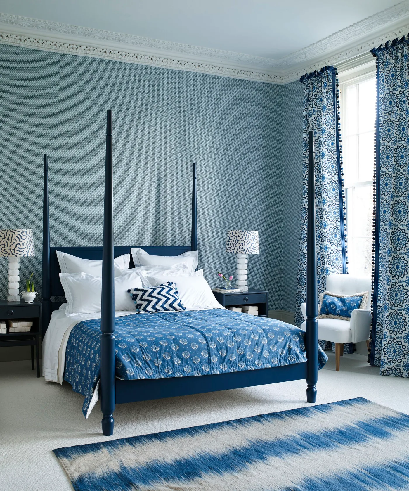Dark blue four-poster bed with patterned blue curtains and bedding, pale walls, and small dark bedside tables.