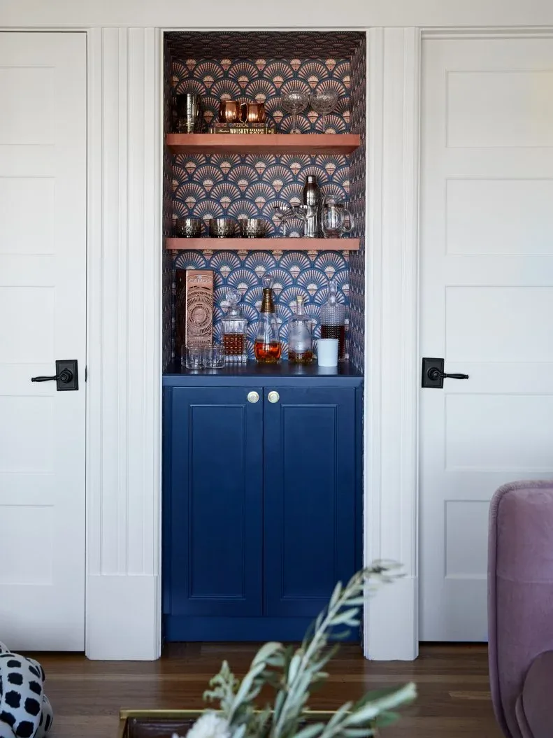 Two reddish wood-toned shelves over a navy drinks cabinet in a patterned niche between white doors