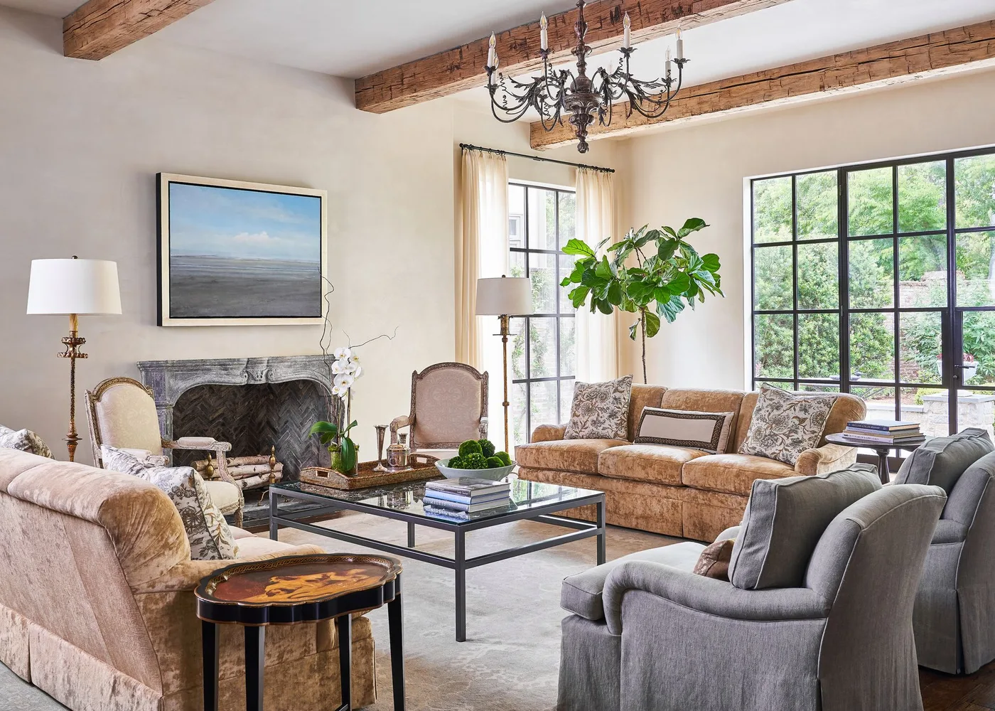 Pale living room with gray curved fireplace surround, landscape picture, exposed wood beams and mixed upholstered seating
