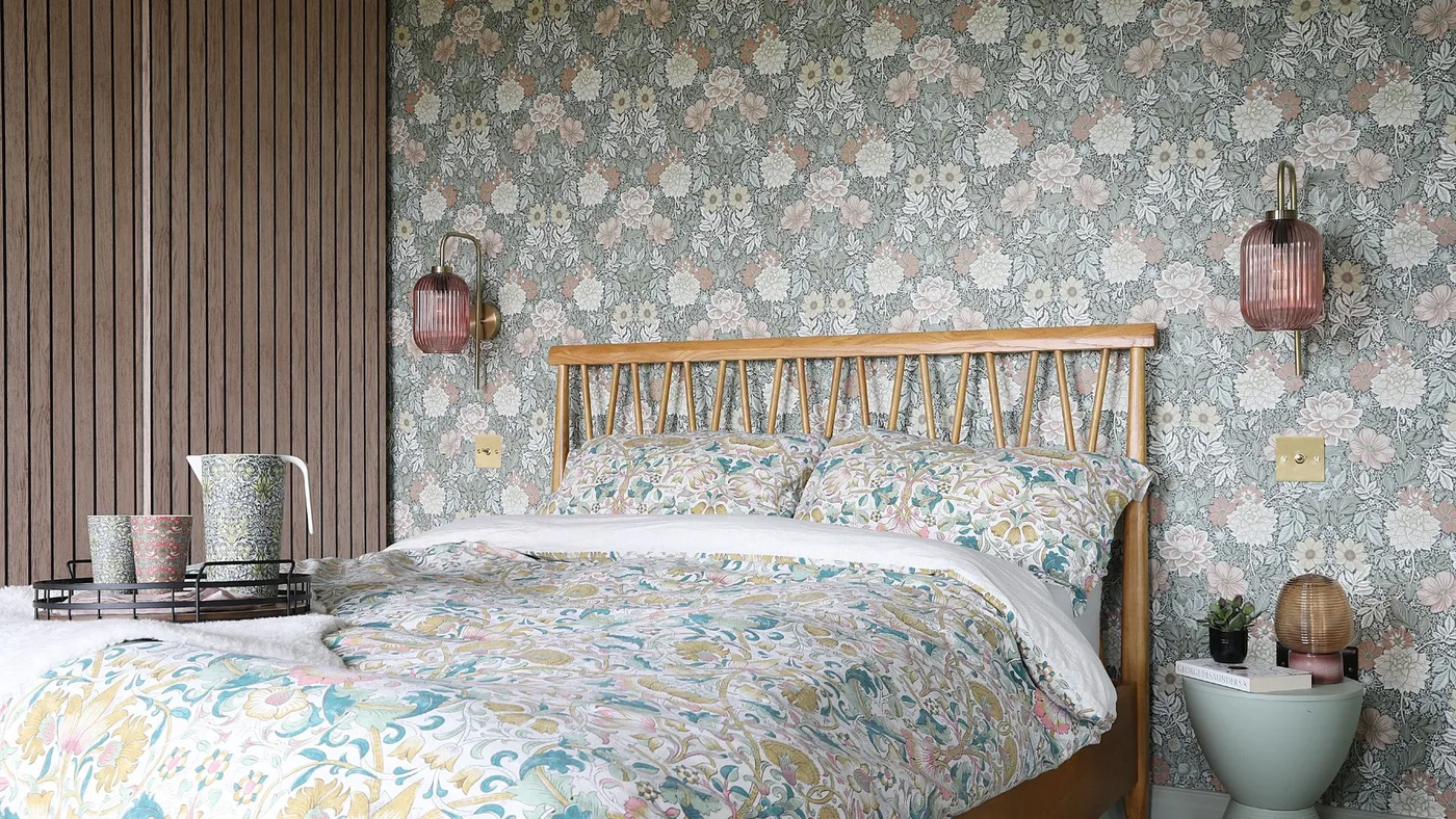 Muted floral wallpaper behind a wooden spindle bed with coordinating floral bedding and a wood slat side wall.