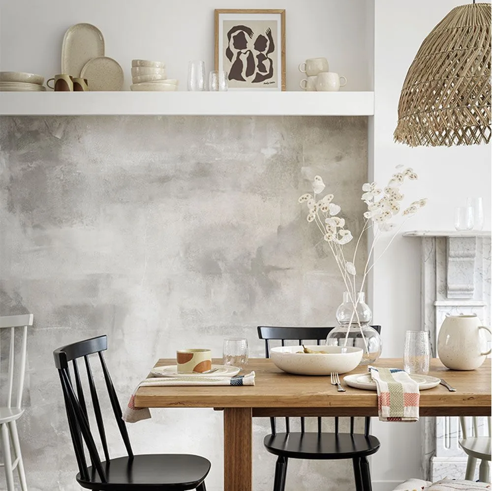 White floating shelf with pale dishes and framed art above a wooden dining table against a mottled gray wall