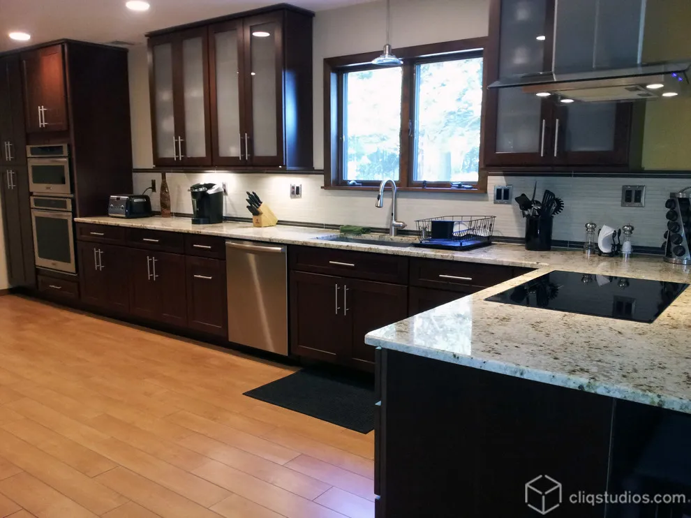 Deep reddish-brown cabinet fronts frame a sink window beside a peninsula with a pale speckled top