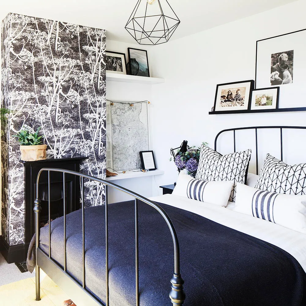 Black-and-white botanical wallpaper sits beside a dark metal bed and pale walls