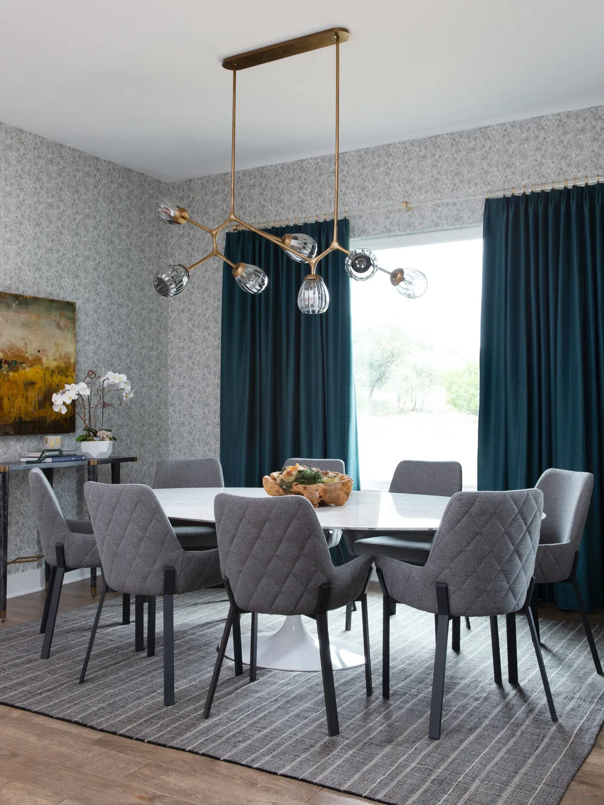 Teal curtains frame a bright window beside patterned walls and gray upholstered chairs.