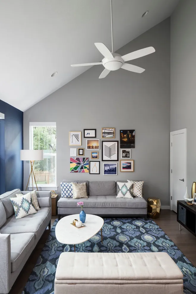 Two gray sofas meet near a blue side wall and a gray gallery wall in a tall living room