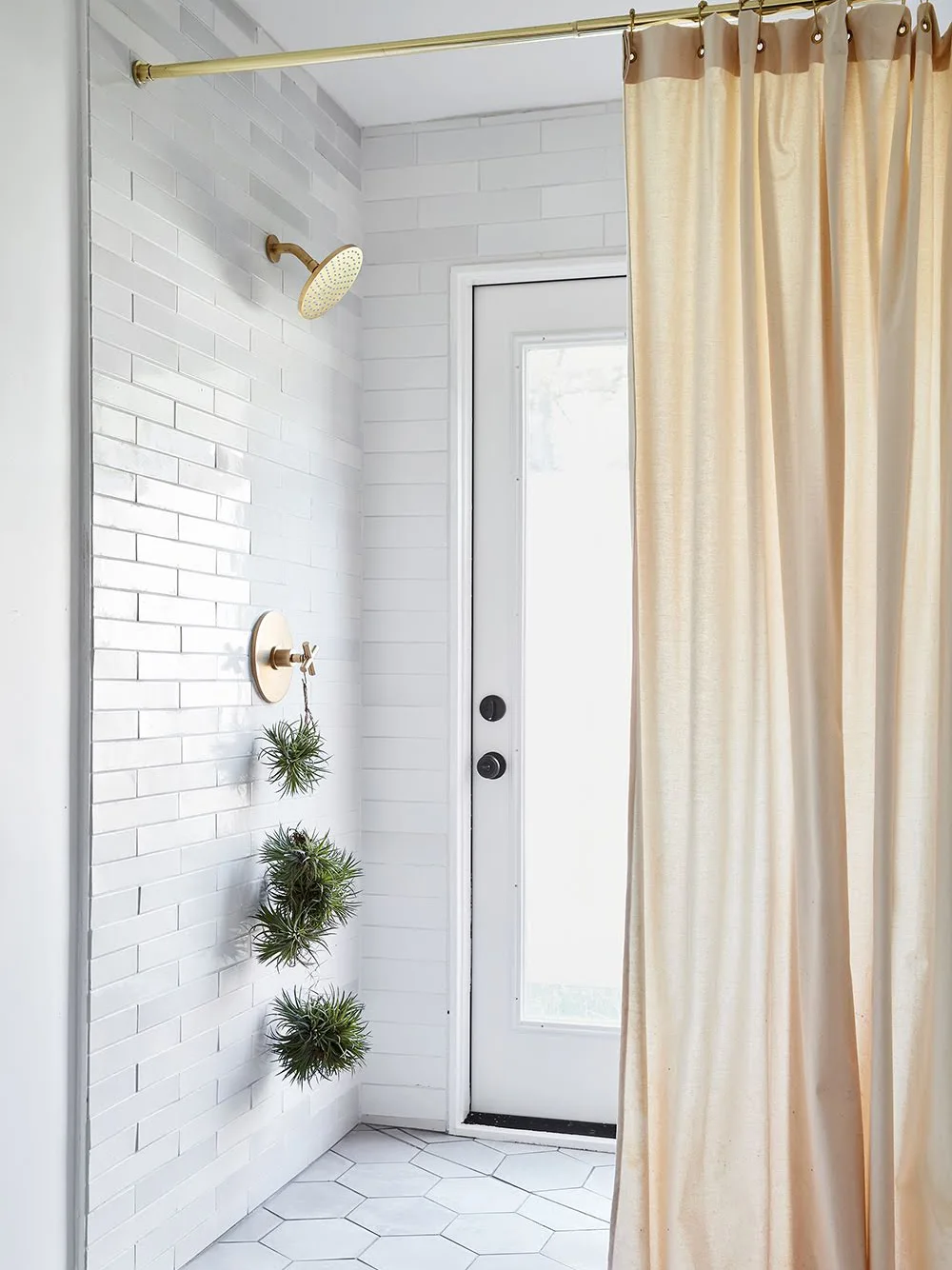 White rectangular shower tiles sit beside a pale curtain, brass-colored fittings and a glazed door