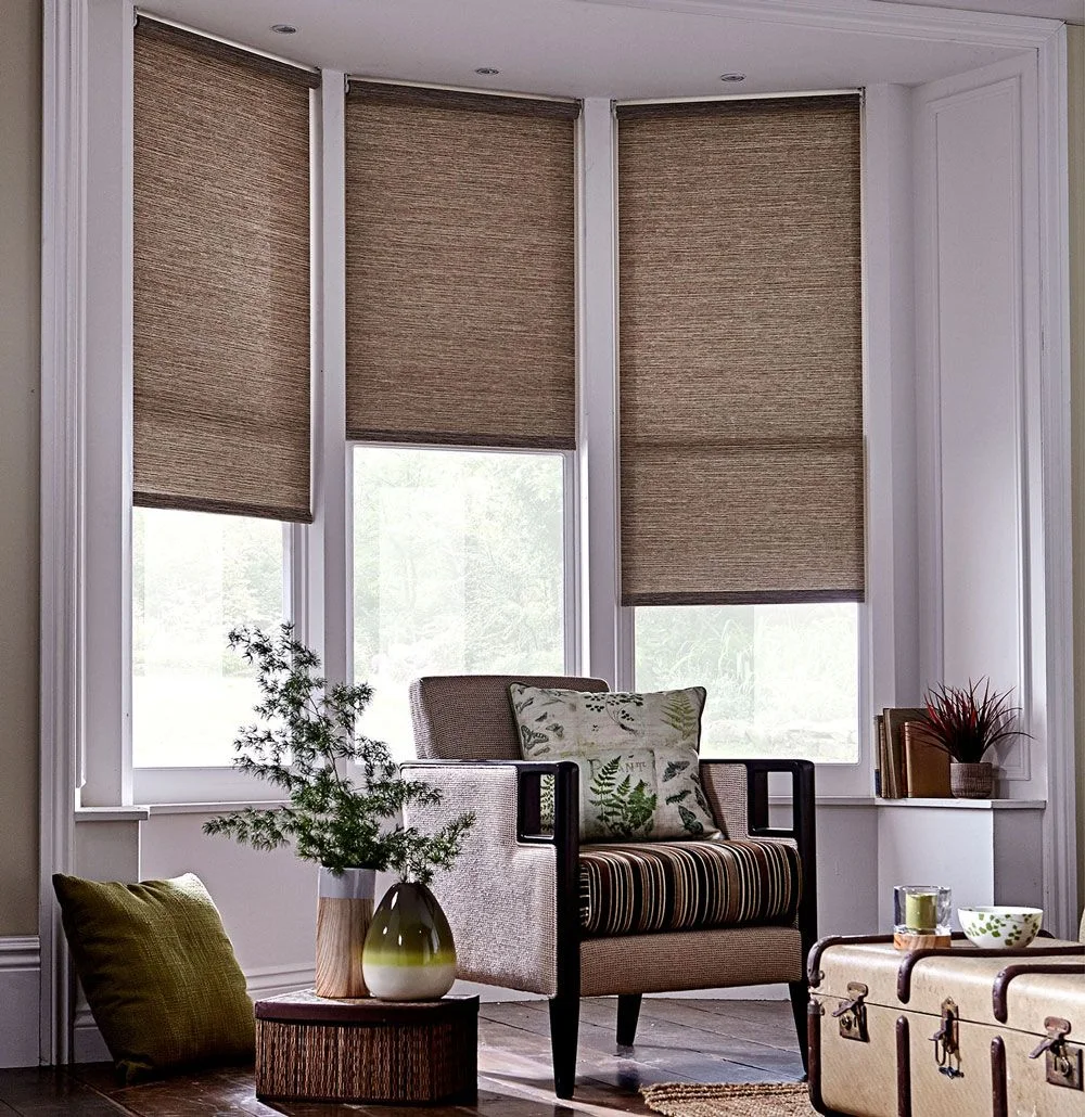 Brown textured blinds frame a chair with a striped seat cushion beside a trunk-style table and smaller wood surface