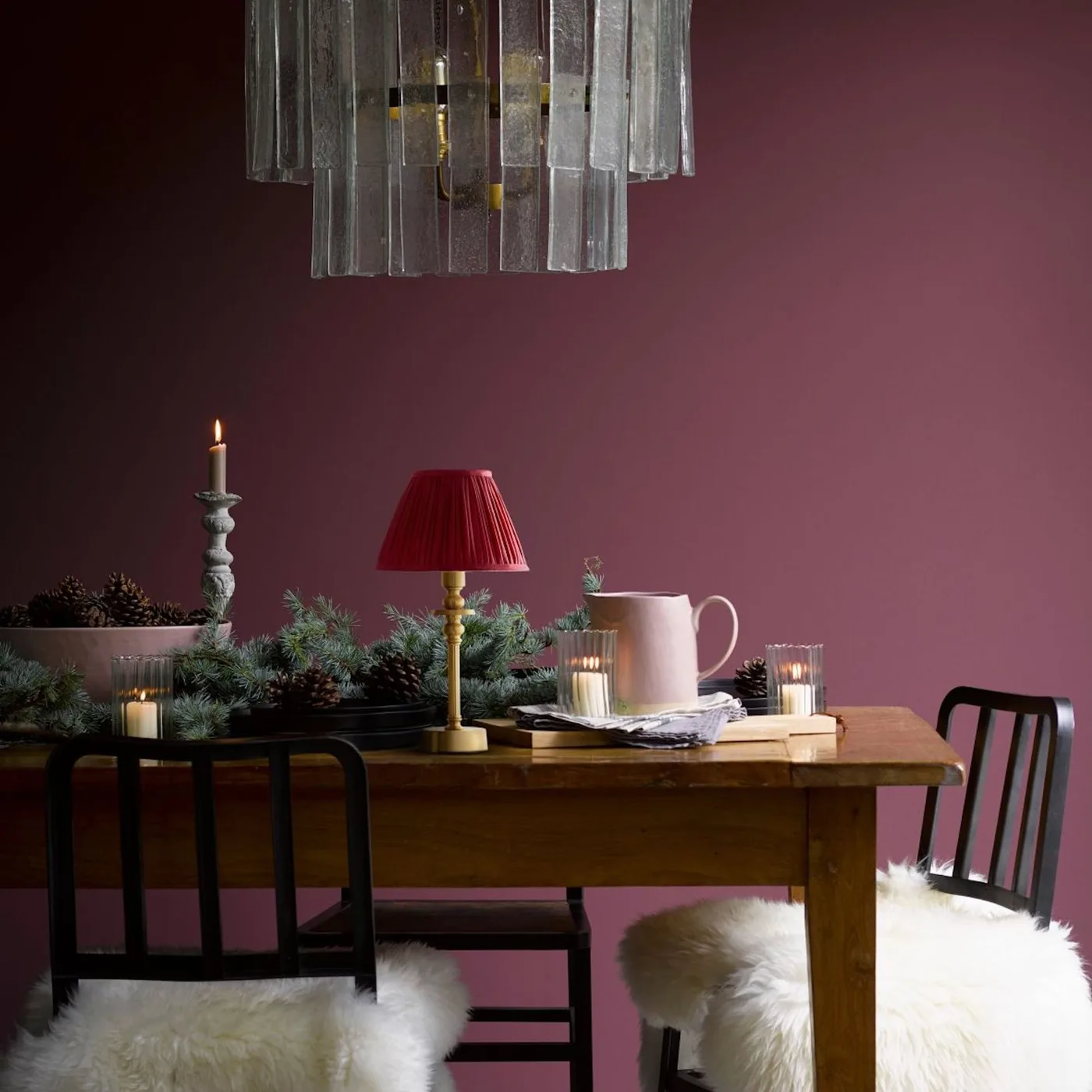 Red pleated table lamp beneath a large hanging light in a raspberry-colored dining room