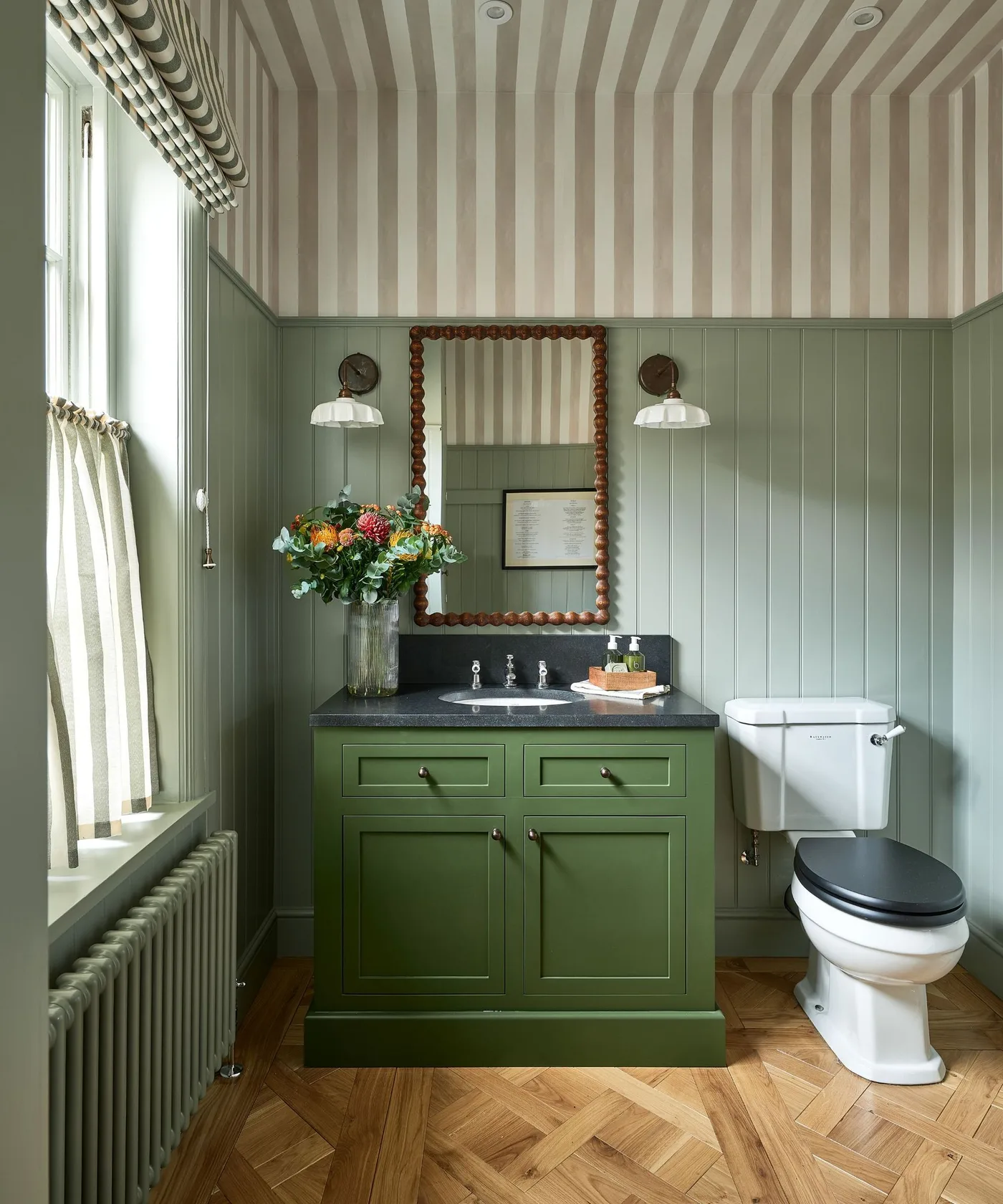 Green paneled powder room with darker green vanity, striped ceiling and pale cafe curtain