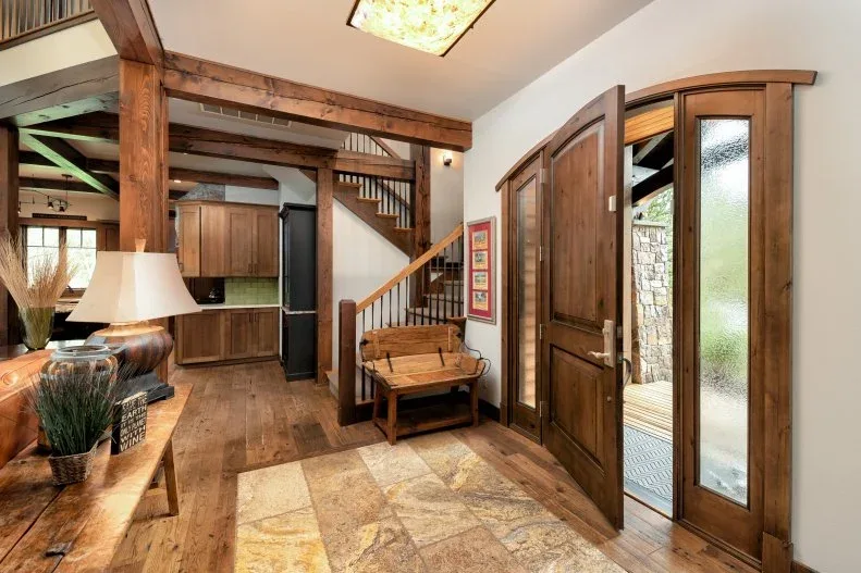 Rustic wood console with tall stems and small objects beside an arched wood door, exposed timbers and a dark bench