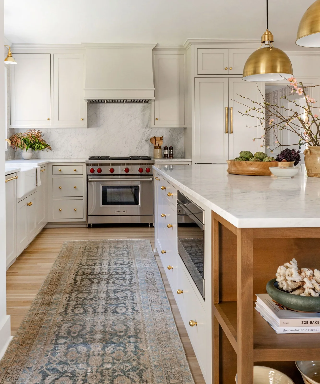 White framed cupboards and a wood-ended island stand beneath warm-toned dome pendants beside pale veined backsplash panels and simple matching handles