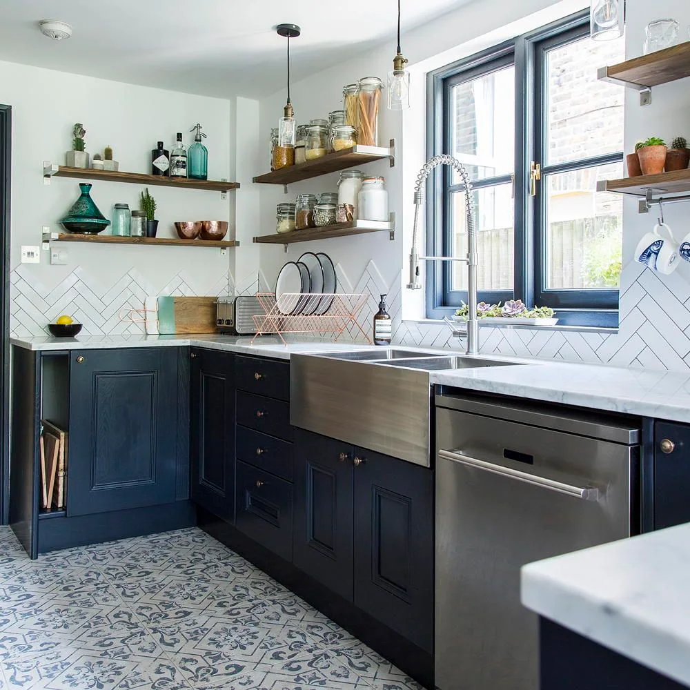 White herringbone backsplash tiles sit above dark kitchen cabinets beside patterned floor tiles and wooden shelves