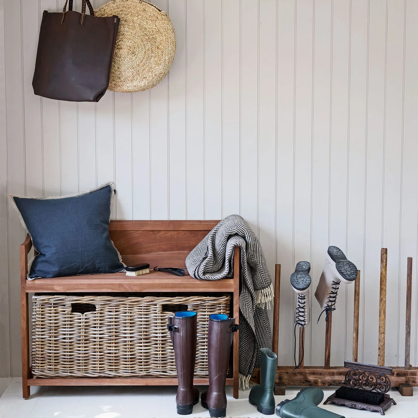 Wood bench with backrest, large lower woven basket, blue cushion, hanging bag and hat, boots and boot-removal aids