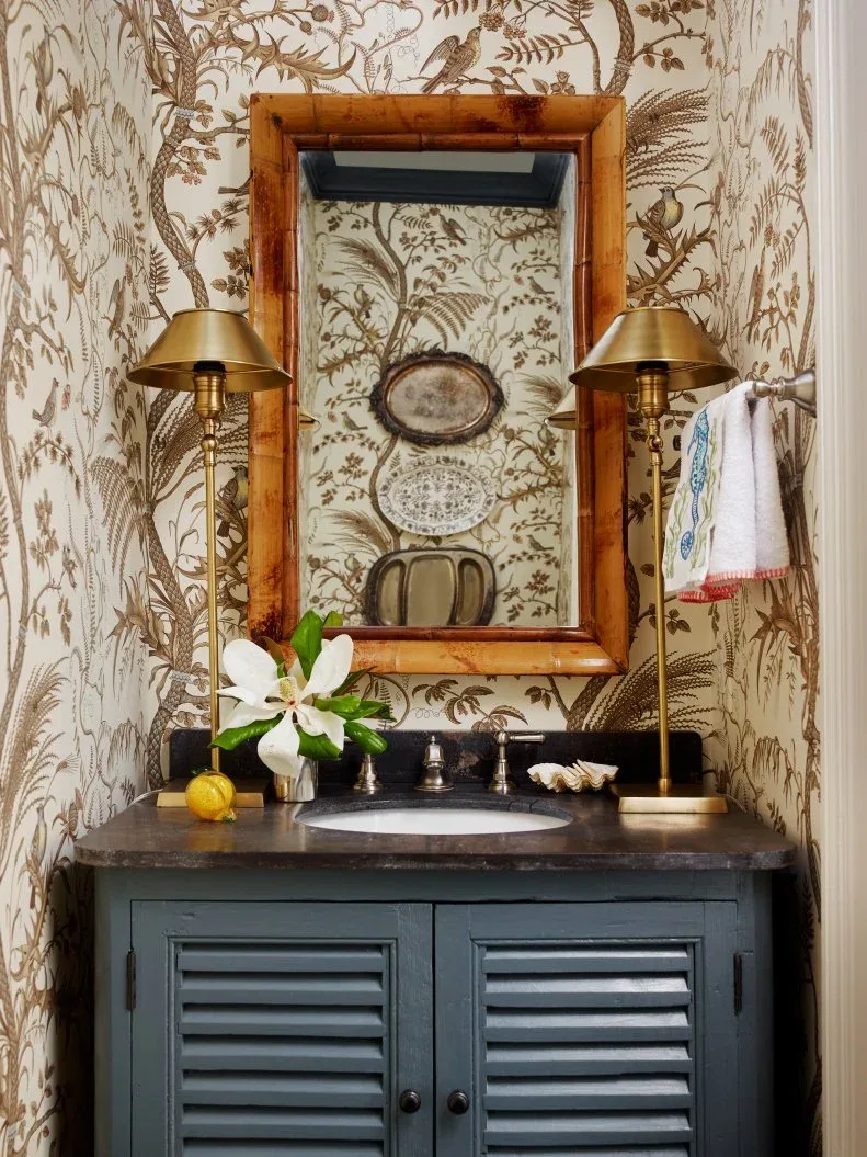 Powder room with brown botanical wallpaper, wood-framed mirror and dark blue louvered vanity