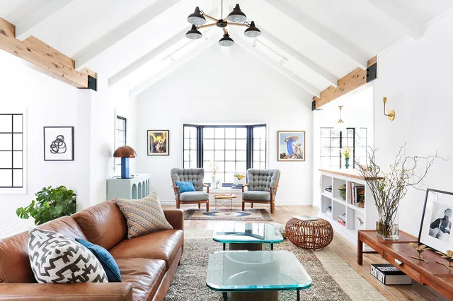 A warm leather sofa sits below a pale pitched ceiling beside blue accents and woven pieces.
