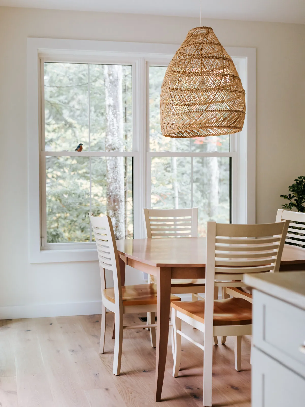 A woven pendant hangs above a small timber table beside a bright window.