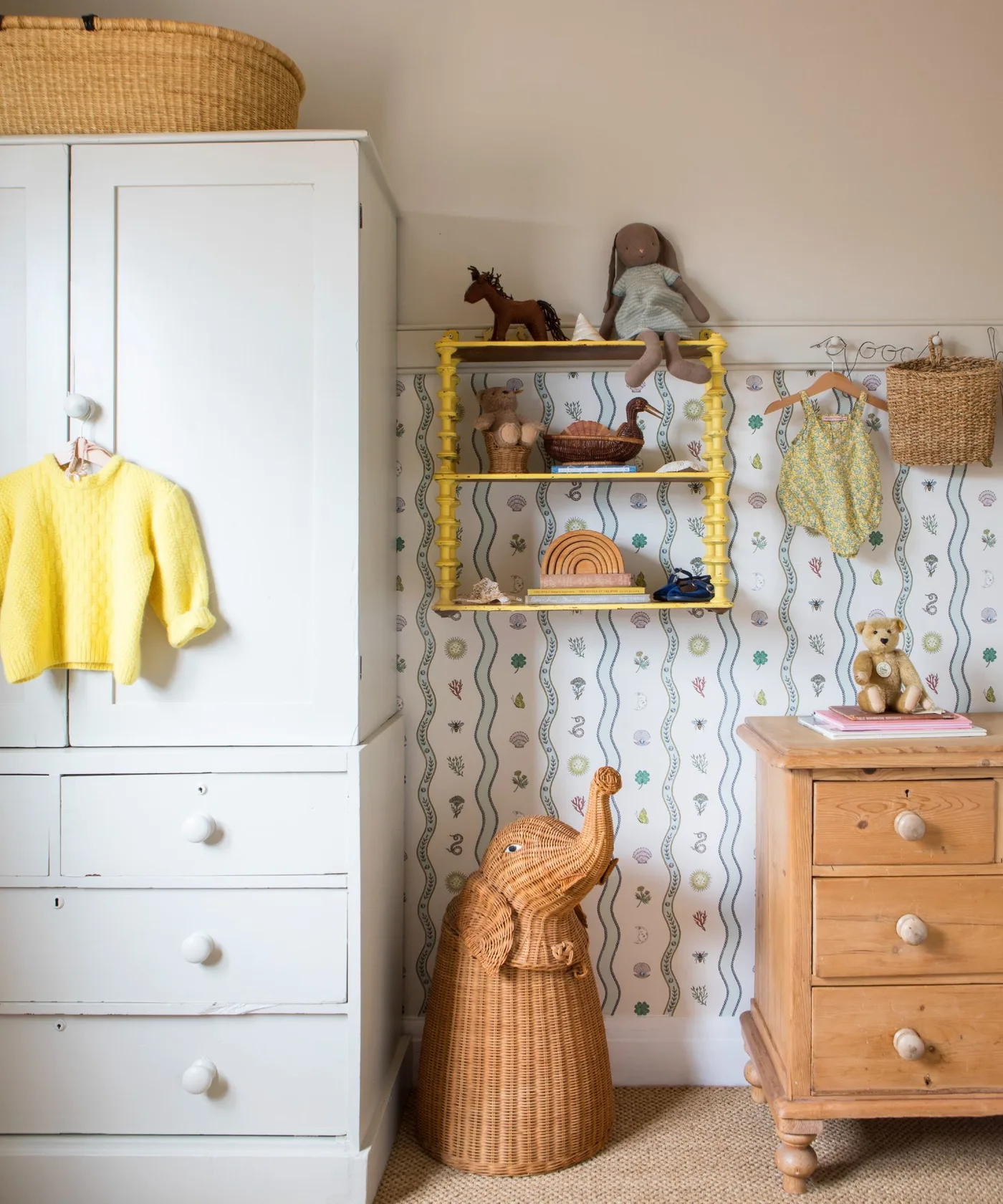 White wardrobe beside warmer wooden dresser against finer lower-wall wallpaper with yellow shelf and smaller woven details.