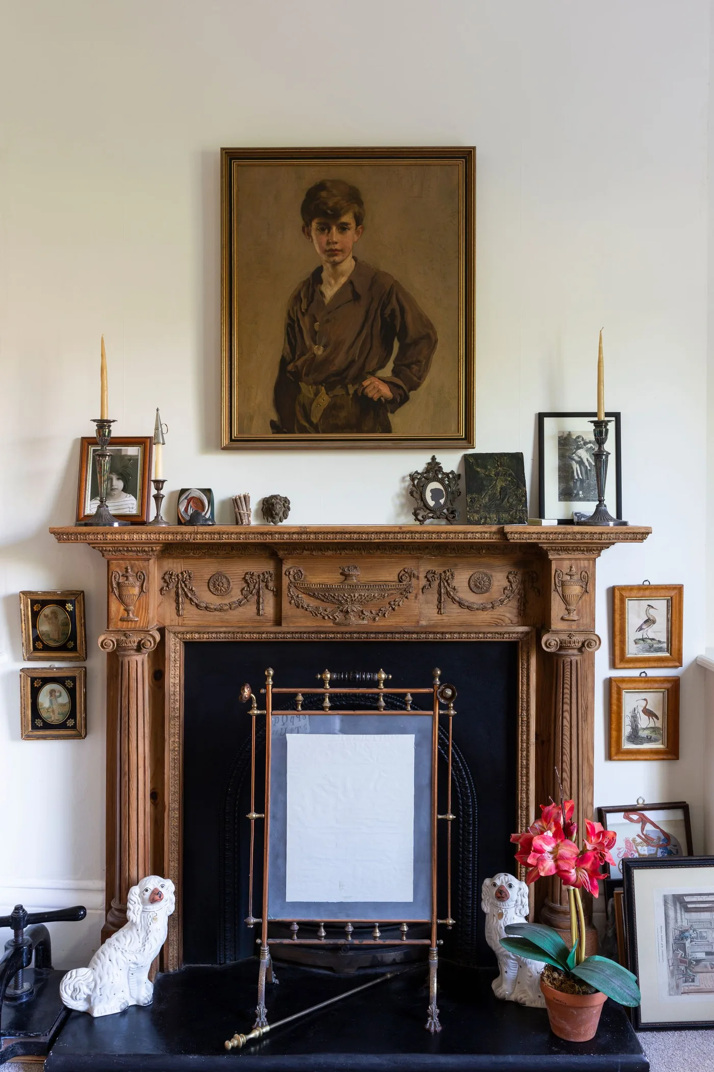 Carved wood fireplace with portrait, rectangular decorative screen, two white dog figures and potted orchid