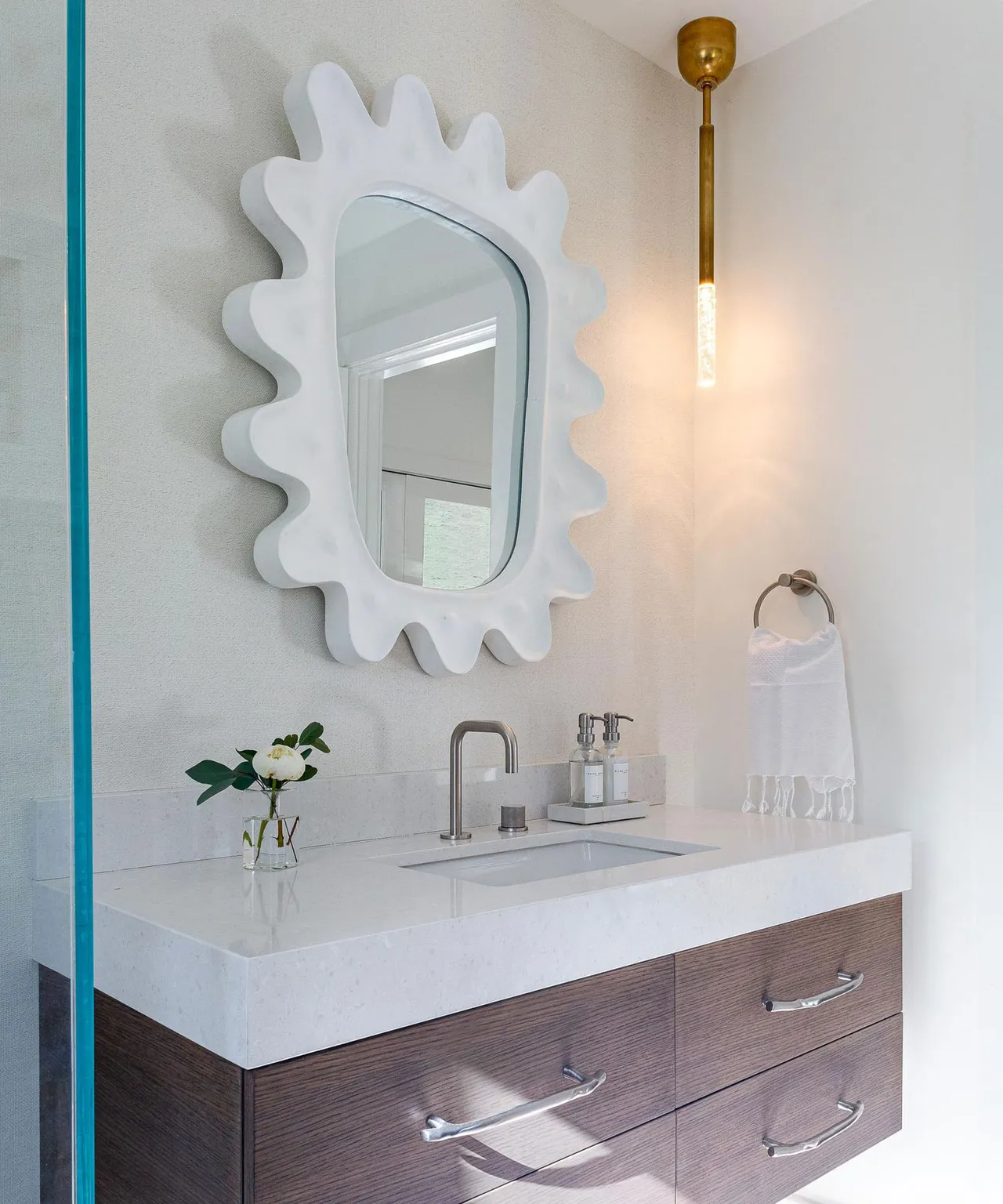 A pale decorative mirror hangs above a straightforward basin and muted vanity.