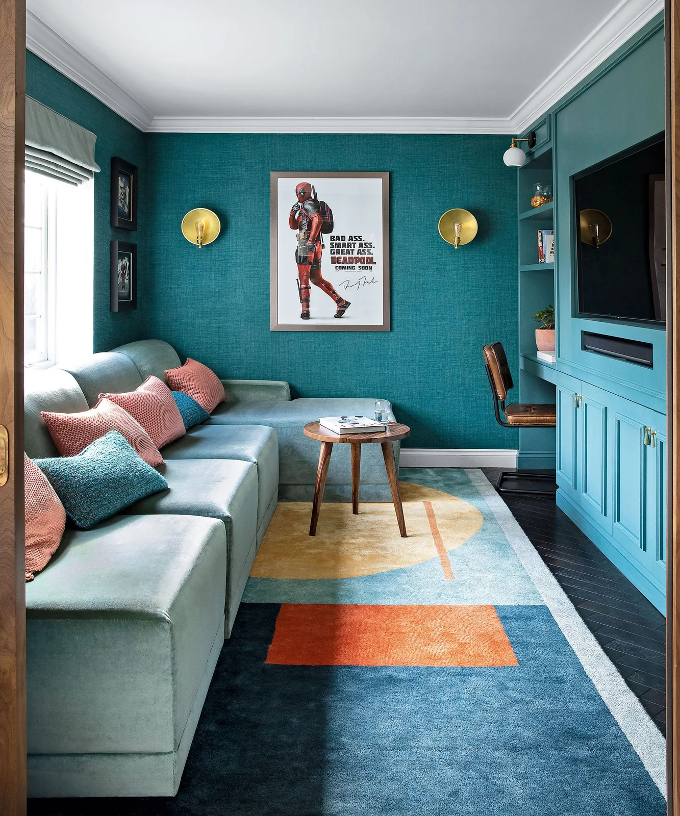 A recessed television and soundbar sit within blue-green cabinets opposite a pale corner sofa beneath gold-toned wall lights