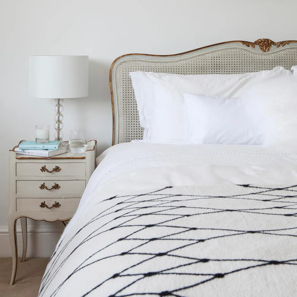 Thin dark lines cross a white bedcover beside a pale traditional headboard