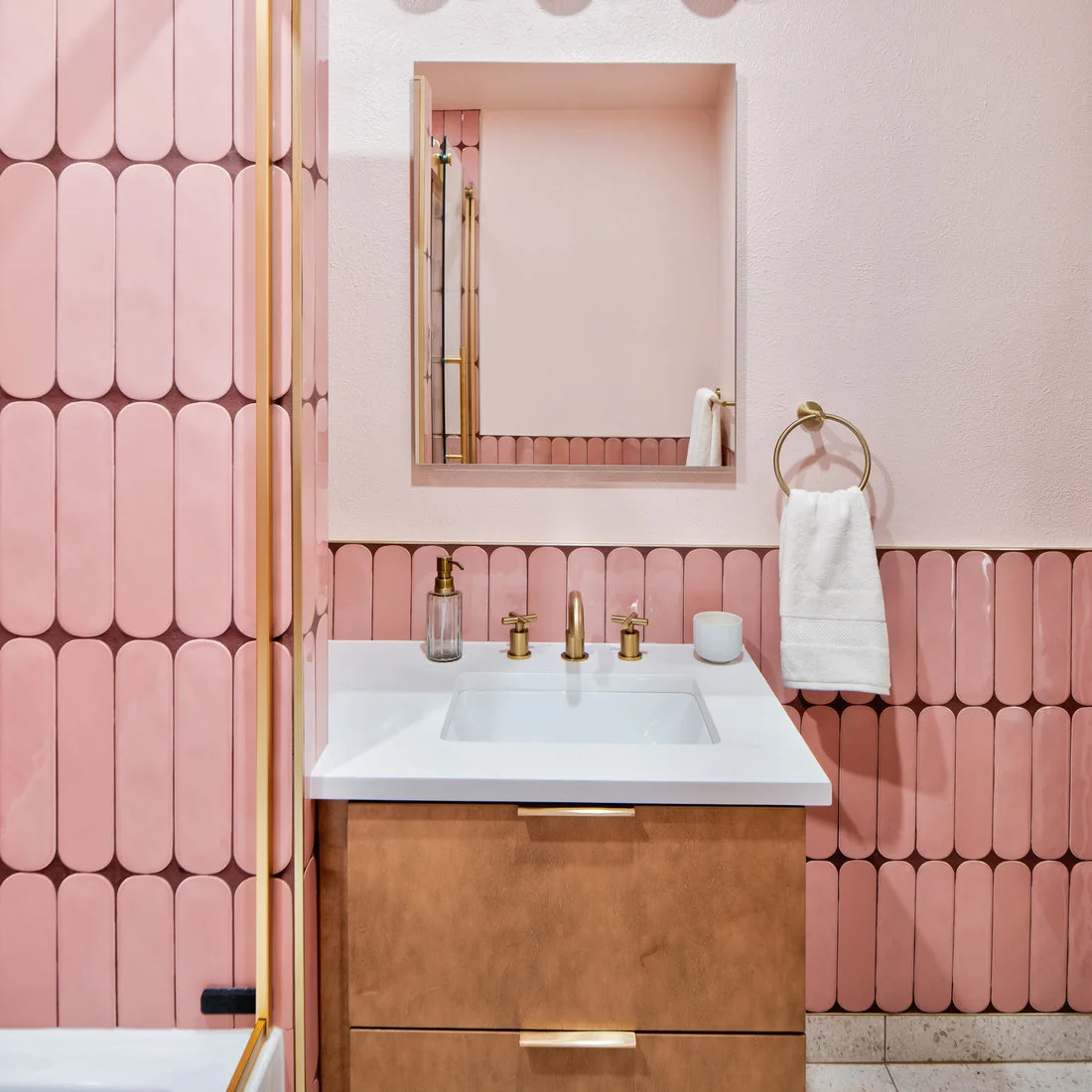 Rounded pink tiles with dark outlines surround a pale sink above wooden drawers and below a rectangular mirror